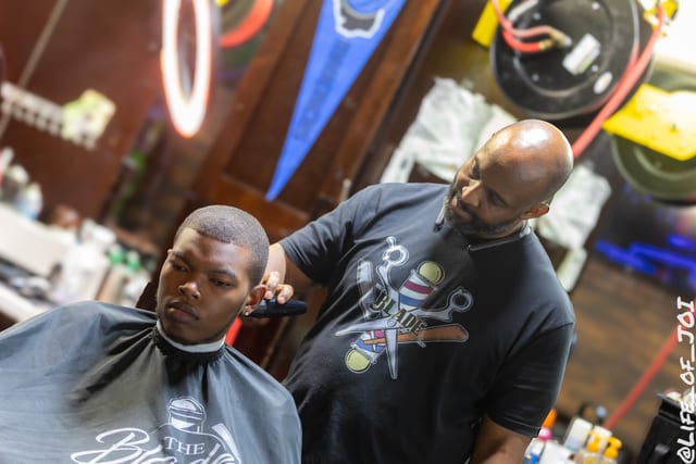 A Blade Barber Lounge barber lines up a young client under the neon ring light during the 888 Fresh Start Experience.