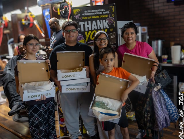 A Las Vegas family holds new Converse sneaker boxes and school supplies in front of the 888 Foundation thank you banner.