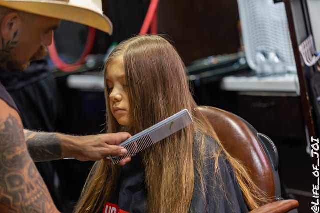 A barber combs out a girl’s long hair during the free girls’ hairstyling offered at the event.