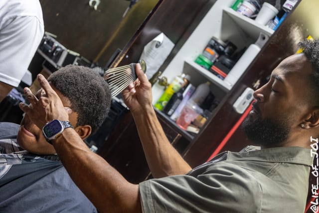 A barber holds up the mirror so a young client can see his finished cut.