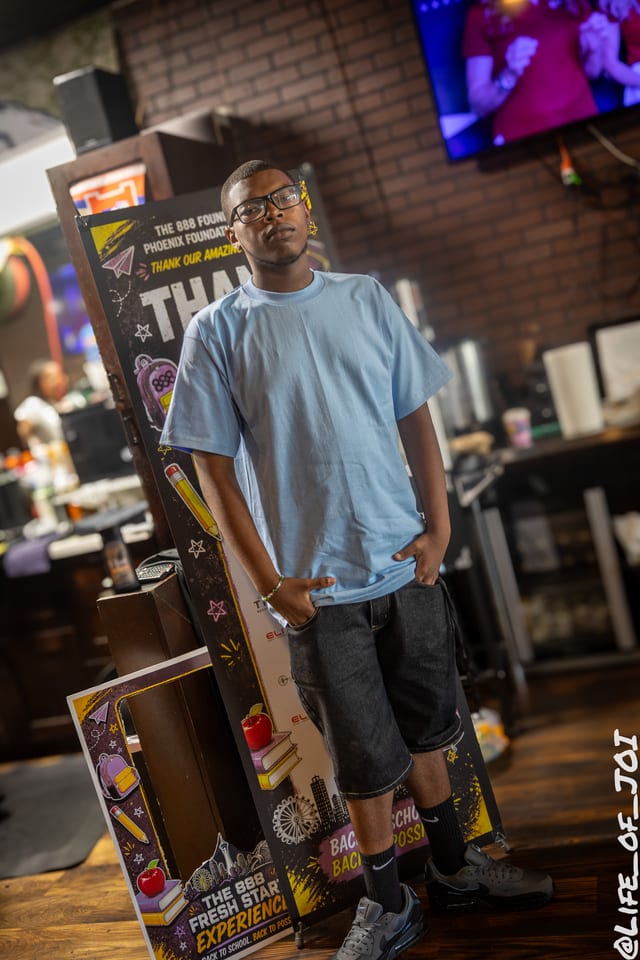 A student stands in front of the 888 Fresh Start Experience banner with his new school gear.