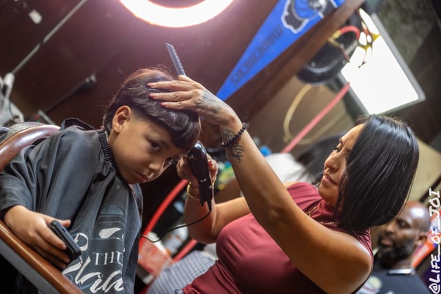 A stylist runs clippers through a student’s hair while he waits in the chair.
