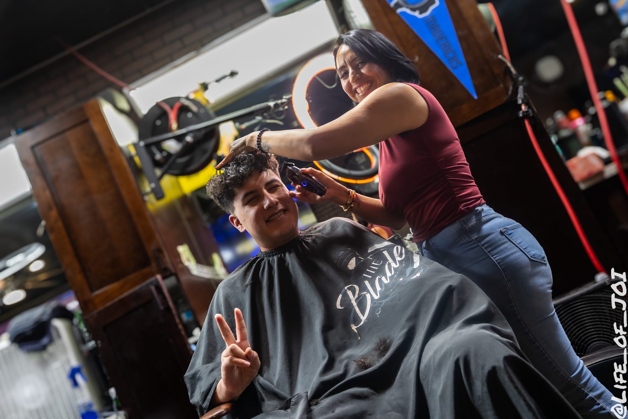 A teenager throws a peace sign from the chair while a stylist finishes his cut.
