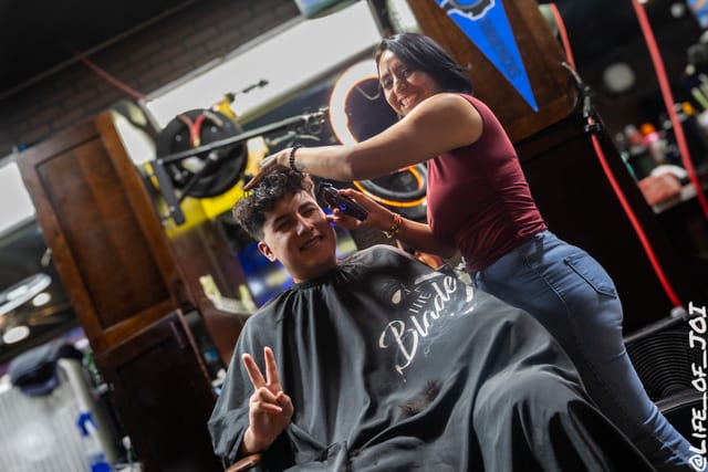 A teenager throws a peace sign from the chair while a stylist finishes his cut.
