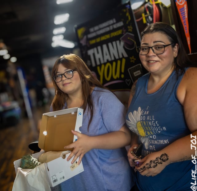 A mother and daughter smile together holding the sneakers and supplies they received.