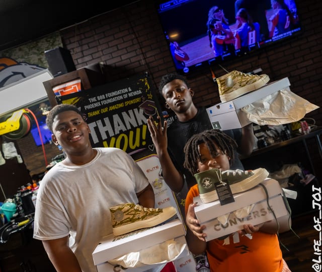 Three kids show off the new sneakers they picked up at the back to school giveaway.